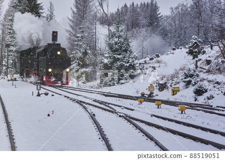 Steam locomotive with smoking and steaming chimney is heading for the snowy switches of the tracks in the forest in winter time Steam locomotive with smoking and steaming chimney is heading for the snowy switches of the tracks in the forest in winter time 88519051