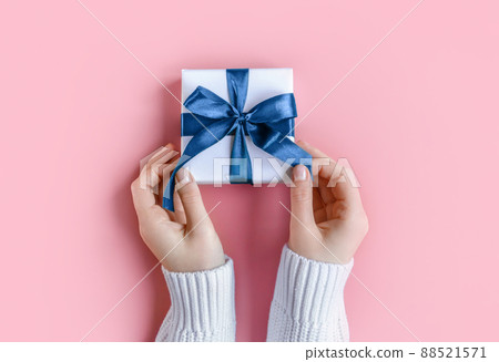 Female Hands in sweater holding gift in white wrapping paper on pink background. St. Valentines Day, Mothers' Day, love, friendship, Birthday, Christmas concept. Cozy, festive, romantic wallpaper 88521571
