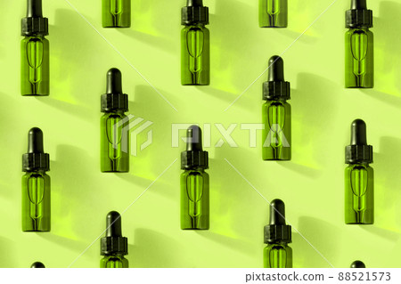 Transparent glass dropper bottle with green liquid inside on light background in the sunlight. Pipette with fluid hyaluronic acid, serum, retinol. Cosmetics, healthcare, beauty  88521573