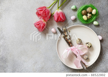 Festive Easter table setting with painted eggs, spring flowers and cutlery on light grey tabletop. Table setting for Happy Easter day. 88522802