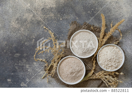 Food and baking ingredient. Wheat flour coarse from whole wheat grains, wheat bran and wheat flour over gray stone background. Top view flat lay. Copy space. 88522811