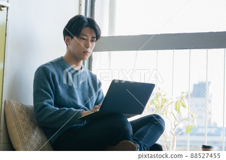 一個年輕人坐在地板上，在電腦上工作 88527455