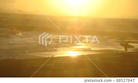 千葉稻毛海岸的夕陽照亮了一個衝浪者在回家的路上拿著衝浪板的身影 88527847