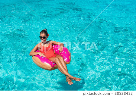 Happy beach summer travel vacation girl sun tanning in red swimsuit having fun relaxing in donut float toy for swimming pool. Blue turquoise water background 88528452