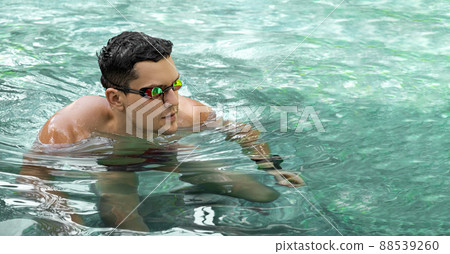 Swimmer. Young athletic brunette man wearing swimming goggles in pool. Panorama banner. Healthy lifestyle. Serious athlete against background of turquoise water. Sports and fitness cardio exercises. Swimmer. Young athletic brunette man wearing swimming goggles in pool. Panorama banner. Healthy lifestyle. Serious athlete against background of turquoise water. Sports and fitness cardio exercises. 88539260