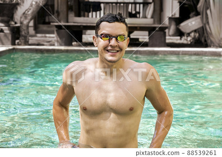 Swimmer. Portrait of smiling athletic man with bare torso wearing glasses for swimming in pool, looking into the camera. Concept of sports, a healthy lifestyle. Sports and fitness cardio exercises. 88539261