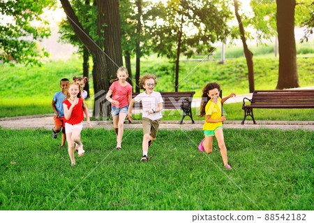 a group of preschoolers running on the grass against the background of the park and greenery. Children Protection Day. 88542182