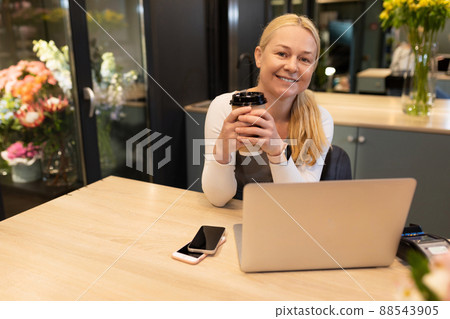 a salesman in a flower shop works at a computer with a cup of coffee in his hands and looks at the 88543905