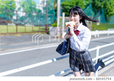 一個似乎遲到了,早餐帶著麵包跑的高中女生。上學遲到的女孩。遲到的麵包女孩。 一個似乎遲到了,早餐帶著麵包跑的高中女生。上學遲到的女孩。遲到的麵包女孩。 88545754