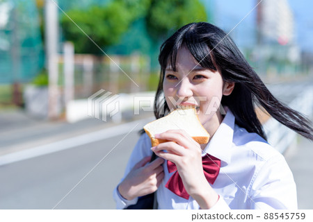 A high school girl who seems to be late and runs with bread for breakfast. A girl who is late for school. A bread girl who is late. 88545759