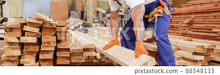 Handsome male builder holding wooden plank at construction site 88548115