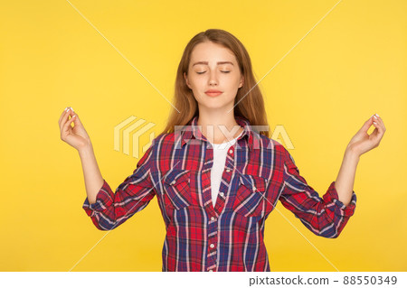 Harmony and inner peace. Portrait of happy calm ginger girl in checkered shirt practicing yoga, holding hands in namaste gesture, meditating with closed eyes. studio shot isolated on yellow background Harmony and inner peace. Portrait of happy calm ginger girl in checkered shirt practicing yoga, holding hands in namaste gesture, meditating with closed eyes. studio shot isolated on yellow background 88550349