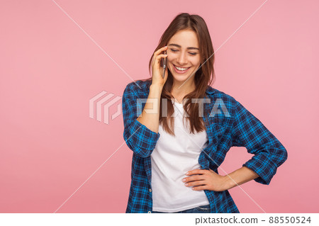 Mobile communication. Happy smiling girl in checkered shirt calling to friend telling good news, expressing positive emotions while talking on cellphone. indoor studio shot isolated on pink background 88550524
