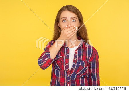 I won't tell anyone. Portrait of scared ginger girl in checkered shirt covering mouth with hand and looking frightened at camera, intimidated female afraid to talk. studio shot, yellow background I won't tell anyone. Portrait of scared ginger girl in checkered shirt covering mouth with hand and looking frightened at camera, intimidated female afraid to talk. studio shot, yellow background 88550556