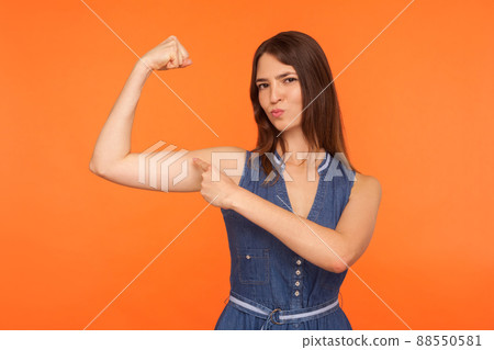 I'm strong and independent. Confident brunette woman pointing to biceps, looking proudly at camera, feeling power and strength to achieve success. indoor studio shot isolated on orange background 88550581