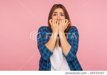 Anxiety. Portrait of scared girl in checkered shirt biting nails fingers and looking terrified, having depression and nervous problem, panic attack. indoor studio shot isolated on pink background 88550587