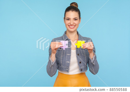 Fascinating joyful fashionably dressed woman with hair bun holding colorful pieces of puzzle, two parts of one, symbol of connection and union, association. studio shot isolated on blue background 88550588