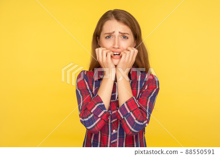 Panic and anxiety. Portrait of worried stressed ginger girl in shirt biting nails, looking scared at camera, suffering depression phobia, terrified about problems. indoor studio shot yellow background Panic and anxiety. Portrait of worried stressed ginger girl in shirt biting nails, looking scared at camera, suffering depression phobia, terrified about problems. indoor studio shot yellow background 88550591