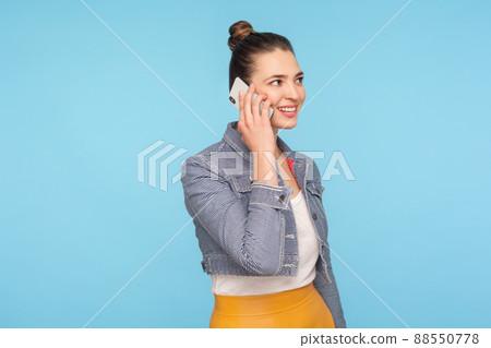 Portrait of beautiful fashionably dressed businesswoman with hair bun talking on cellphone and smiling pleased, discussing good news, happy to communicate on mobile phone. studio shot blue background Portrait of beautiful fashionably dressed businesswoman with hair bun talking on cellphone and smiling pleased, discussing good news, happy to communicate on mobile phone. studio shot blue background 88550778