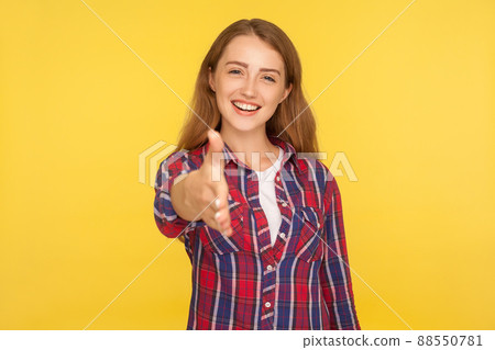 Welcome. Portrait of friendly sociable ginger girl in checkered shirt reaching out hand to camera, offering handshake, greeting and getting acquainted. indoor studio shot isolated on yellow background 88550781