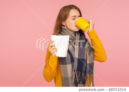 Flu treatment. Portrait of sick ginger girl wearing big scarf, holding napkin and drinking hot tea, treating influenza and high temperature, healthcare. indoor studio shot isolated on pink background Flu treatment. Portrait of sick ginger girl wearing big scarf, holding napkin and drinking hot tea, treating influenza and high temperature, healthcare. indoor studio shot isolated on pink background 88551014