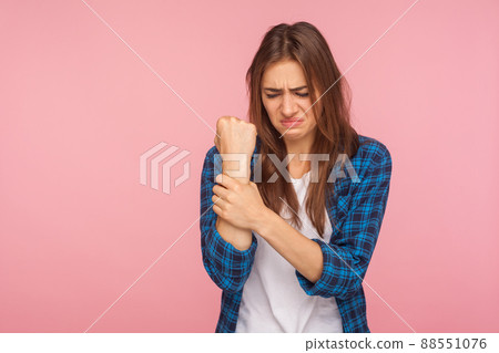 Wrist pain. Portrait of unhappy sick girl in checkered shirt holding her injured hand and grimacing from pain, carpal tunnel syndrome, pinched nerve. indoor studio shot isolated on pink background 88551076