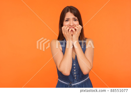 Scared stressed brunette woman biting nails, looking at camera with frightened nervous expression, suffering obsessive-compulsive disorder, anxiety. indoor studio shot isolated on orange background 88551077