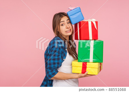 Portrait of funny woman carrying lot of heavy present boxes falling on her, looking with comical surprised grimace, trying to hold many birthday gifts. indoor studio shot isolated on pink background 88551088