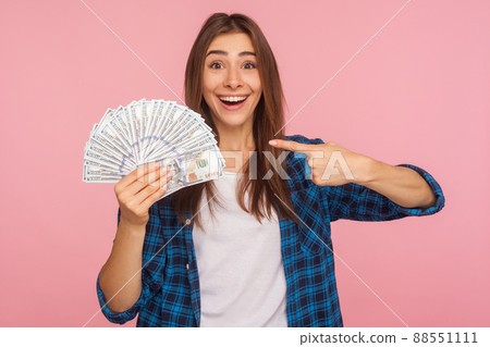 Portrait of joyful lucky girl in casual shirt happy to hold lot of money, pointing at dollar bills in hand and smiling excitedly, enjoying lottery win. indoor studio shot isolated on pink background Portrait of joyful lucky girl in casual shirt happy to hold lot of money, pointing at dollar bills in hand and smiling excitedly, enjoying lottery win. indoor studio shot isolated on pink background 88551111