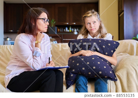 Woman social worker talking to girl child at home, making notes on clipboard. 88553135