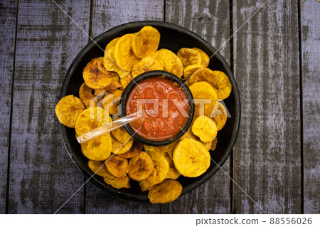 Plantain chips served with Colombian traditional hogao on top of a wooden table 88556026