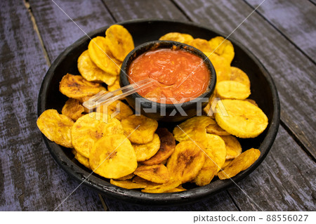 Plantain chips served with Colombian traditional hogao on top of a wooden table 88556027