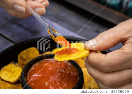 Closeup of woman's hands while eating plantain chips served with Colombian traditional hogao 88556029