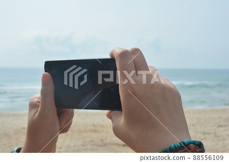 Woman holding landscape smartphone with blank screen while On the beach 88556109