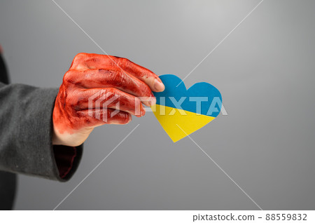 Woman with hands covered in blood holding a heart with the flag of ukraine on a white background.  88559832