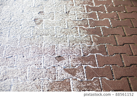 Partially snow-covered red cobblestone sidewalk. Close-up view. Partially snow-covered red cobblestone sidewalk. Close-up view. 88561152