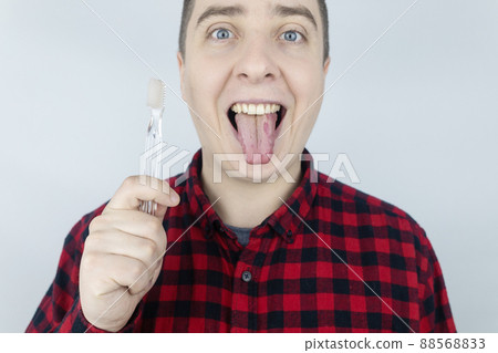 Clean tongue. Close-up of a man performing antimicrobial hygiene with a special tongue brush. Isolated on white background. Male looks into the frame, as if he is looking in a mirror. White coating Clean tongue. Close-up of a man performing antimicrobial hygiene with a special tongue brush. Isolated on white background. Male looks into the frame, as if he is looking in a mirror. White coating 88568833