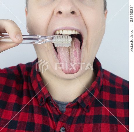 Clean tongue. Close-up of a man performing antimicrobial hygiene with a special tongue brush. Isolated on white background. Male looks into the frame, as if he is looking in a mirror. White coating Clean tongue. Close-up of a man performing antimicrobial hygiene with a special tongue brush. Isolated on white background. Male looks into the frame, as if he is looking in a mirror. White coating 88568834