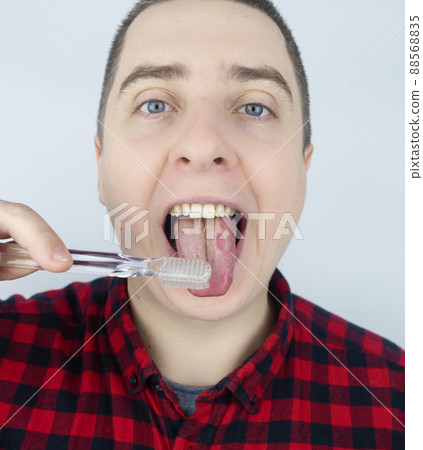 Clean tongue. Close-up of a man performing antimicrobial hygiene with a special tongue brush. Isolated on white background. Male looks into the frame, as if he is looking in a mirror. White coating 88568835