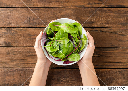 Overhead shot of woman hands holding green salad in bowl on rustic wooden background. Close up Overhead shot of woman hands holding green salad in bowl on rustic wooden background. Close up 88569997