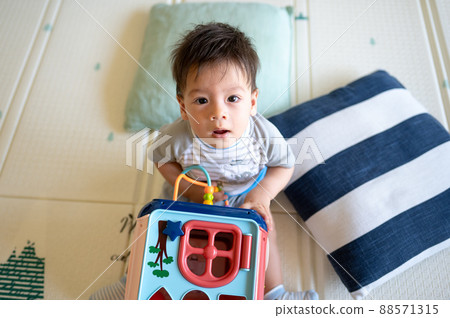Baby boy playing with activity box in the bedroom while sitting on the floor Baby boy playing with activity box in the bedroom while sitting on the floor 88571315