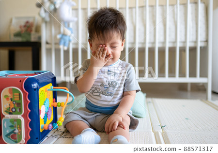 Baby boy playing with activity box in the bedroom while sitting on the floor 88571317