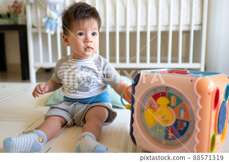 Baby boy playing with activity box in the bedroom while sitting on the floor 88571319