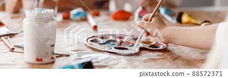 Child hand painting on paper with two classmate in the background Child hand painting on paper with two classmate in the background 88572371