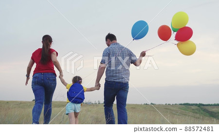 child kid runs with mother father with beautiful colorful balloons. happy family concept. group people running across field with helium colored balloons. happy family running green field together. 88572481