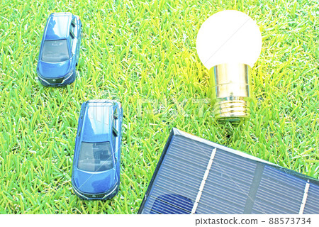Two hydrogen cars placed on the lawn, a shining light bulb and a solar panel 88573734
