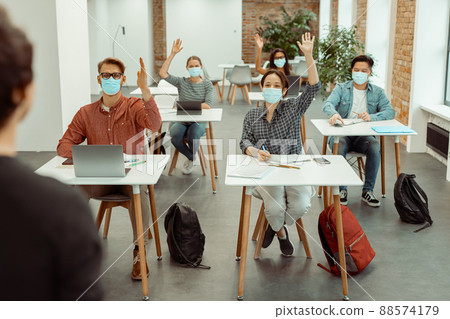Students in facial protective mask raising hand for answer 88574179