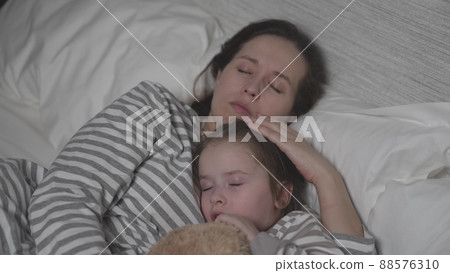 Small daughter and mother lie in bed trying to fall asleep 88576310