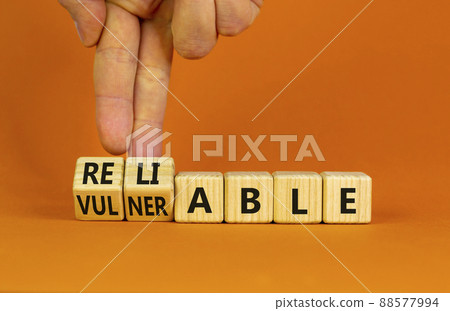 Vulnerable or reliable symbol. Businessman turns wooden cubes and changes the word Vulnerable to Reliable. Beautiful orange background, copy space. Business and vulnerable or reliable concept. 88577994
