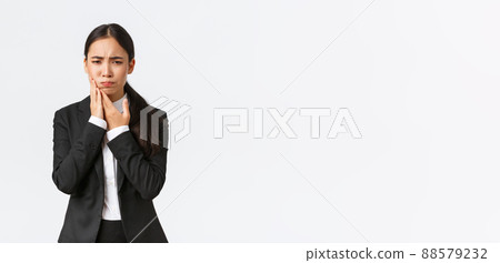 Female asian office manager in black suit having toothache at work. Troubled businesswoman holding hand on cheek as feeling pain in teeth, need appointment doctor, standing white background Female asian office manager in black suit having toothache at work. Troubled businesswoman holding hand on cheek as feeling pain in teeth, need appointment doctor, standing white background 88579232